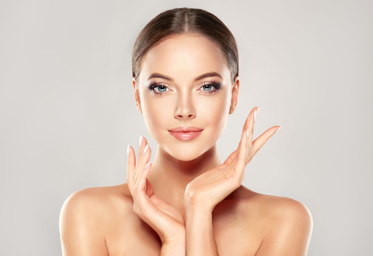 Beauty-Aufnahme einer Frau, die direkt in die Kamera schaut und mit den Händen elegant ihr Gesicht rahmt